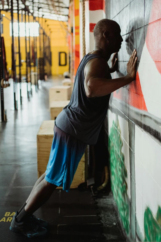 a man leaning against a wall in a gym, by Jessie Algie, pexels contest winner, athletic crossfit build, square, stretching to walls, chromatic