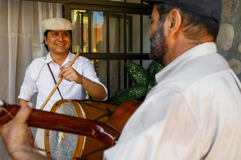 a man playing a musical instrument next to another man, rafeal albuquerque, tamborine, during the day, profile image