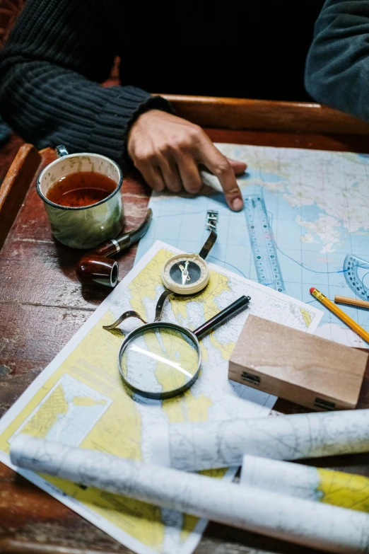 a person sitting at a table with a map and a pair of glasses, explorers, square, brown, curated collections