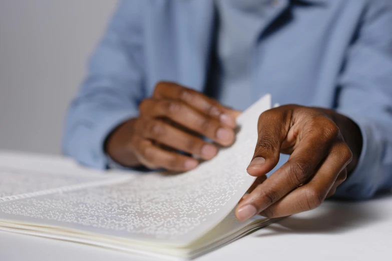 a man sitting at a table reading a book, unsplash, realism, closeup of hand, realistic », jemal shabazz, on vellum