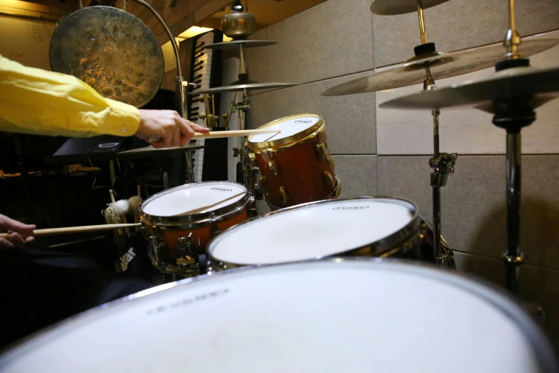 a man in a yellow shirt is playing drums, an album cover, unsplash, photorealism, kyoani studio, b - roll, thumbnail, pov photo