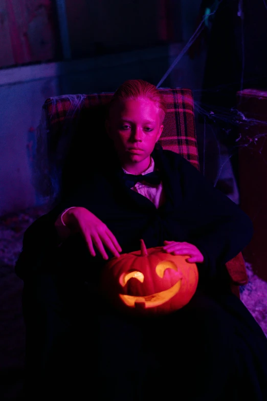 a woman sitting in a chair holding a carved pumpkin, an album cover, inspired by Lasar Segall, inside haunted house, black light, a boy, high-res