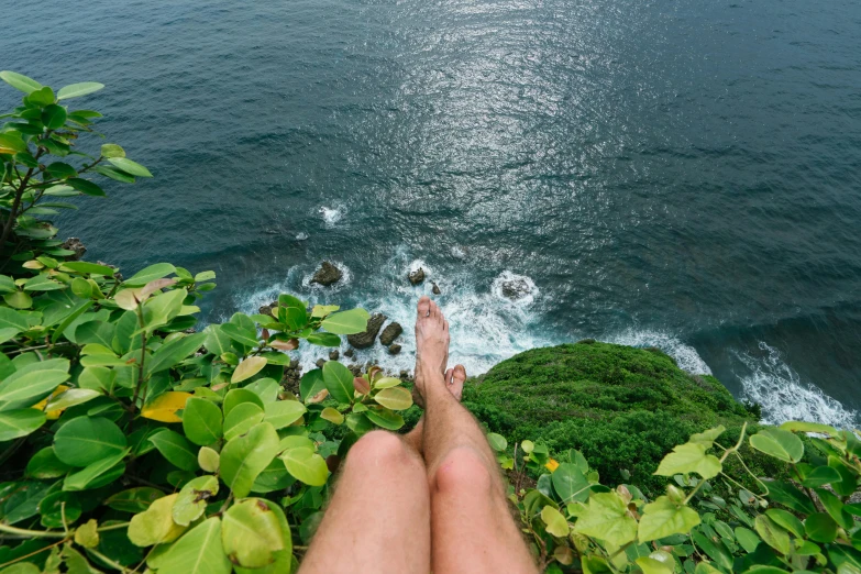 a person sitting on top of a lush green hillside next to the ocean, inspired by Ren Hang, pexels contest winner, hairy legs, bali, micro pov, ultra-realistic