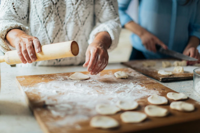 a woman rolling out dough on a cutting board, by Julia Pishtar, pexels contest winner, crispy buns, family photo, te pae, close together