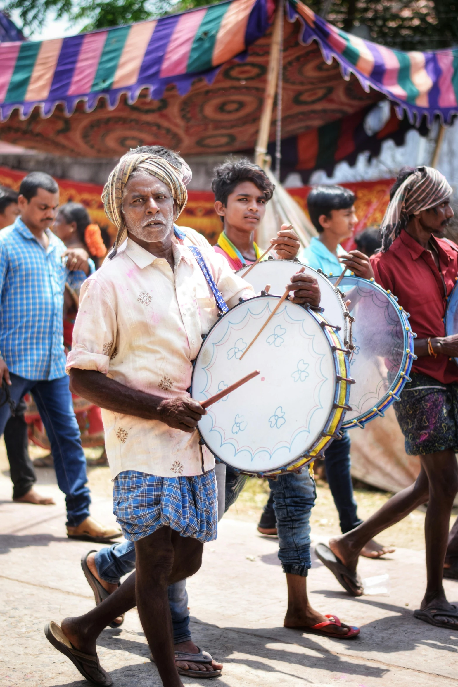 a man holding a drum while walking down a street, an album cover, pexels contest winner, samikshavad, temple fair, a group of people, an oldman, ( ( theatrical ) )