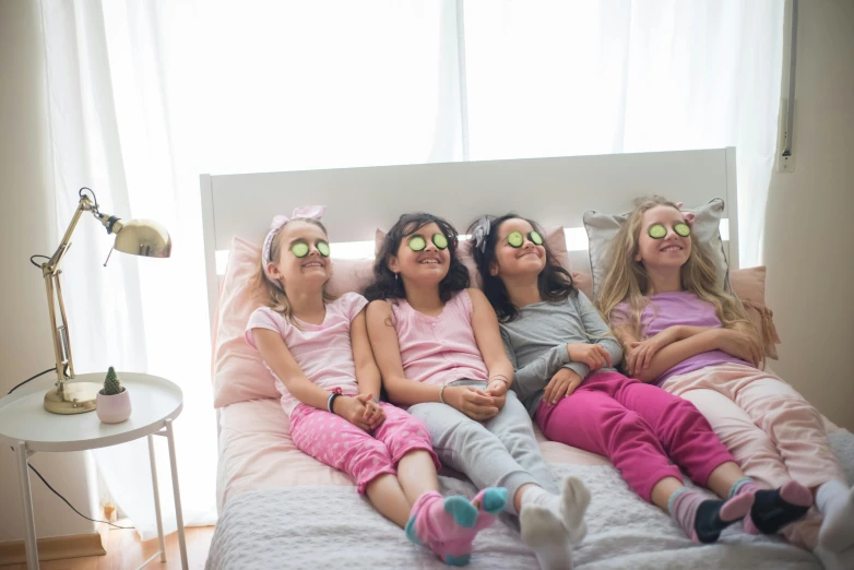 a group of little girls laying on top of a bed, circular glasses, gazing off into the horizon, in the bedroom at a sleepover, promo image