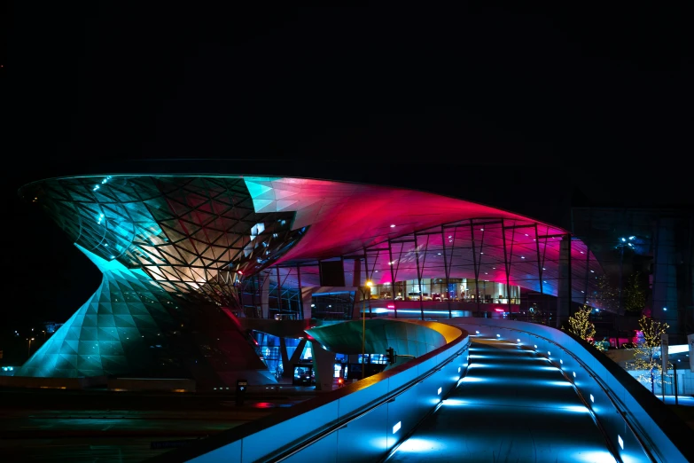 a building that is lit up at night, inspired by Zha Shibiao, unsplash contest winner, magenta and crimson and cyan, sportspalast amphitheatre, car shot, elegantly dressed
