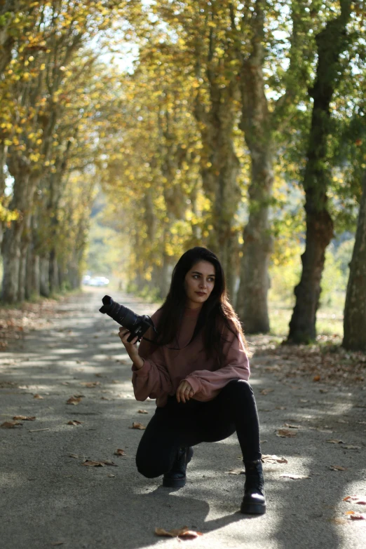 a woman kneeling down with a gun in her hand, by Nazmi Ziya Güran, pexels contest winner, realism, trees in the background, during autumn, medium format. soft light, car shot
