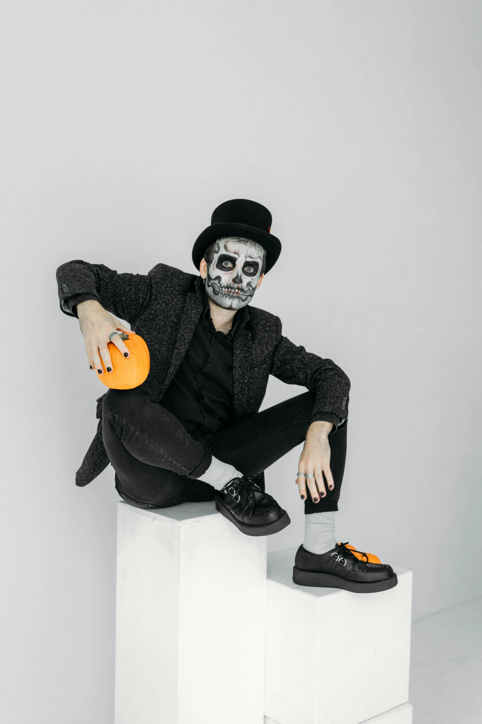 a man dressed as a skeleton sitting on a cube, inspired by Germán Londoño, black and orange colour palette, wearing a bowler hat, with a white background, minimal black skull warpaint