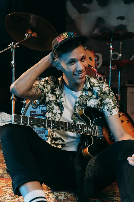 a man that is sitting down with a guitar, he is smiling, bella poarch, medium head to shoulder shot, with index finger