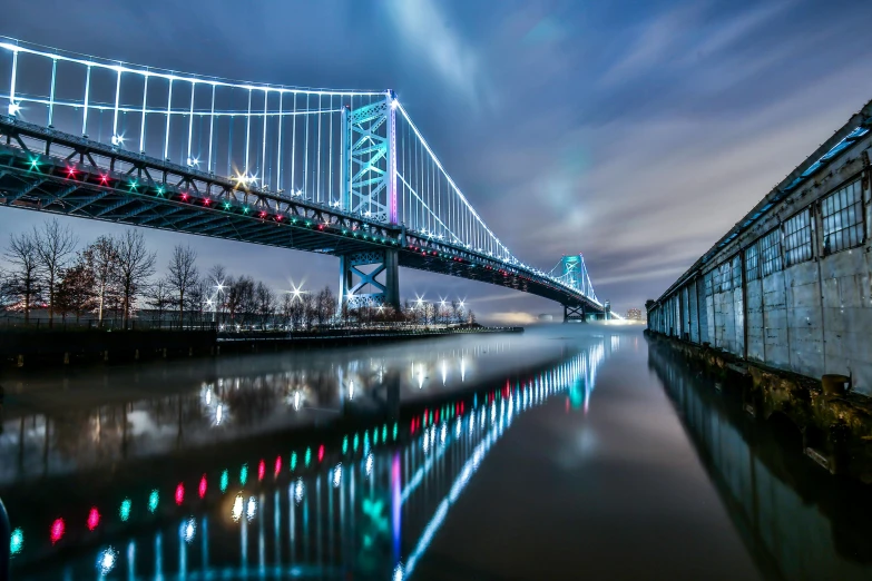 a bridge over a body of water at night, by Jacob Burck, pexels contest winner, teal lights, new jersey, city reflection, colorful photograph