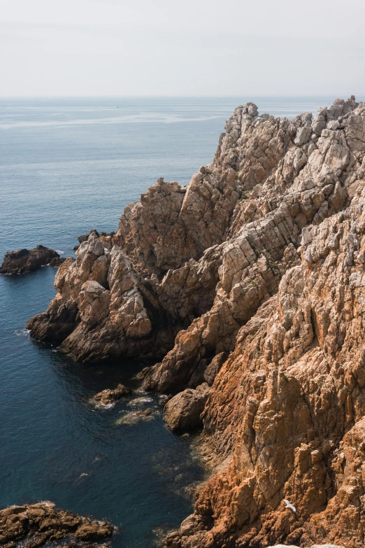 a man standing on top of a cliff next to the ocean, by Carlo Martini, les nabis, gigapixel photo, large rocks, panoramic, brown