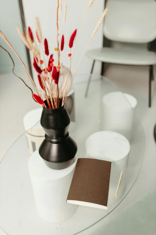 a glass table topped with a vase filled with flowers, by Robbie Trevino, pexels contest winner, modernism, black and terracotta, white candles, white and red color scheme, sustainable materials