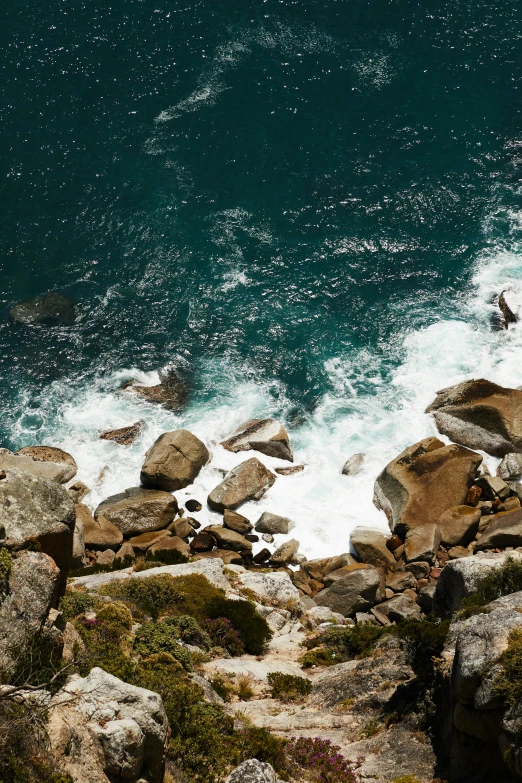 a man standing on top of a rocky cliff next to the ocean, south african coast, slide show, top - down photo, ocean spray