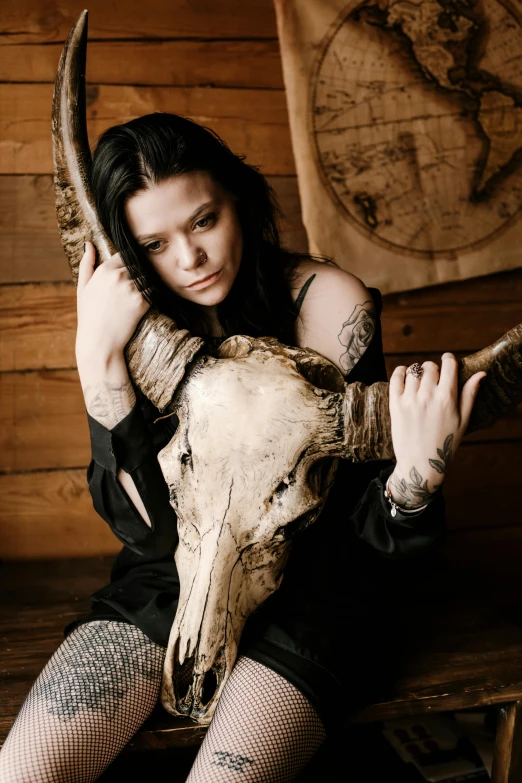 a woman sitting on top of a wooden bench next to a cow skull, raven black hair, promo image, bam margera, holding a wood piece