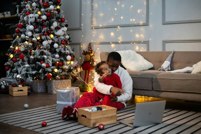 a woman and child sitting on the floor in front of a christmas tree, pexels contest winner, figuration libre, with a laptop on his lap, hugging his knees, mkbhd, lots of decoration and furniture