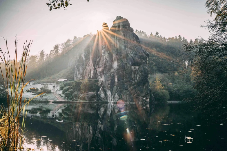 a large rock sitting in the middle of a lake, by Sebastian Spreng, pexels contest winner, romanticism, sun light, forest with lake, tall stone spires, shining lights on cliff side