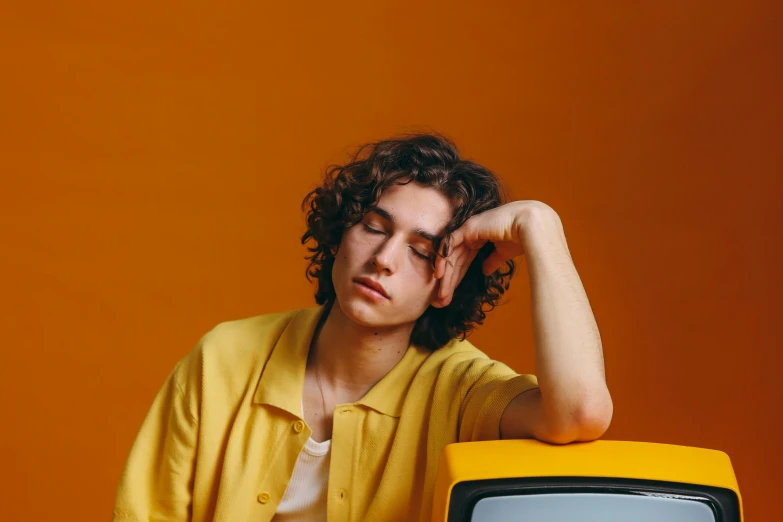 a man sitting in front of a yellow television, an album cover, trending on pexels, photorealism, he has short curly brown hair, sleepy expression, car shot, luca