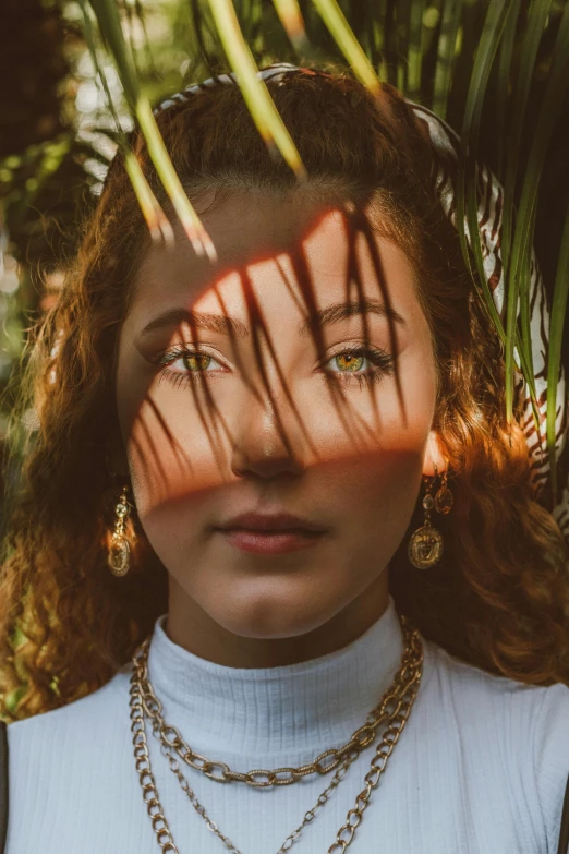 a woman standing in front of a palm tree, an album cover, inspired by Elsa Bleda, trending on pexels, renaissance, gold colored eyes, curly copper colored hair, high angle closeup portrait, portrait sophie mudd