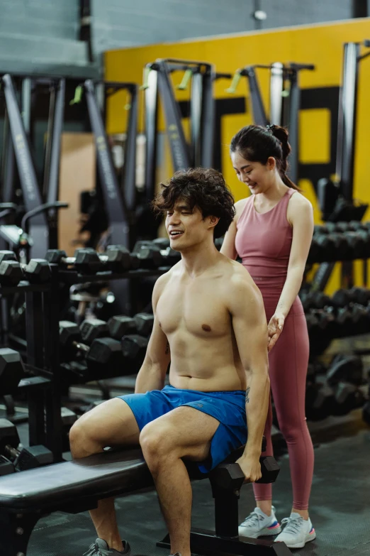 a man and a woman sitting on a bench in a gym, inspired by Adam Dario Keel, pexels contest winner, renaissance, joy ang, serving body, small shoulders, wearing yellow croptop