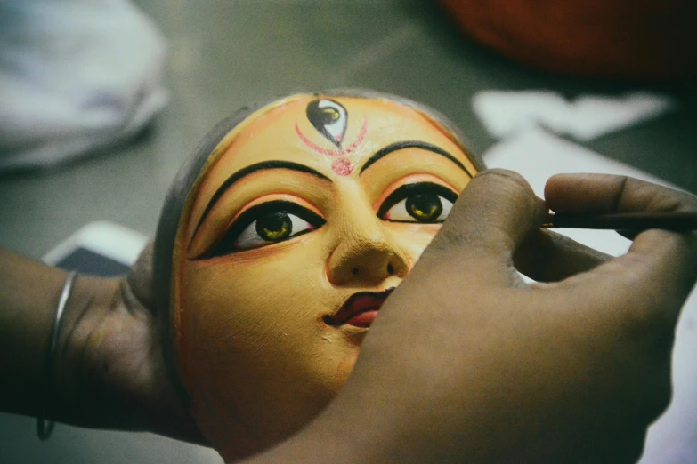 a close up of a person making a mask, bengal school of art, coloured photo, deity), illustration »