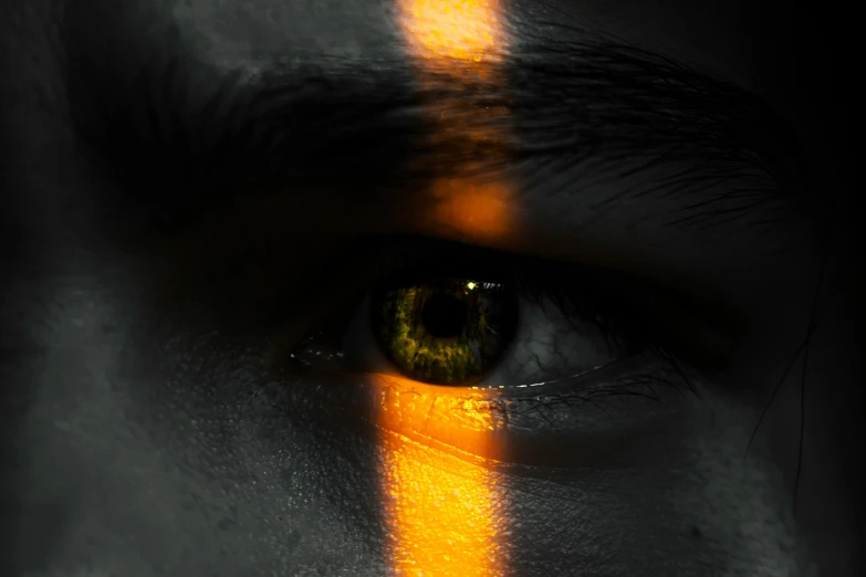 a close up of a person's eye with a cross painted on it, by Adam Marczyński, pexels contest winner, yellow artificial lighting, orange yellow, on a gray background, gold glow