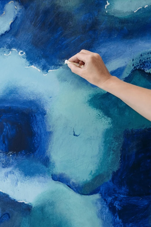 a person holding a paintbrush in front of a painting, an acrylic painting, inspired by Cleve Gray, trending on unsplash, deep blue sea color, 144x144 canvas, ariel view, watercolor on canvas