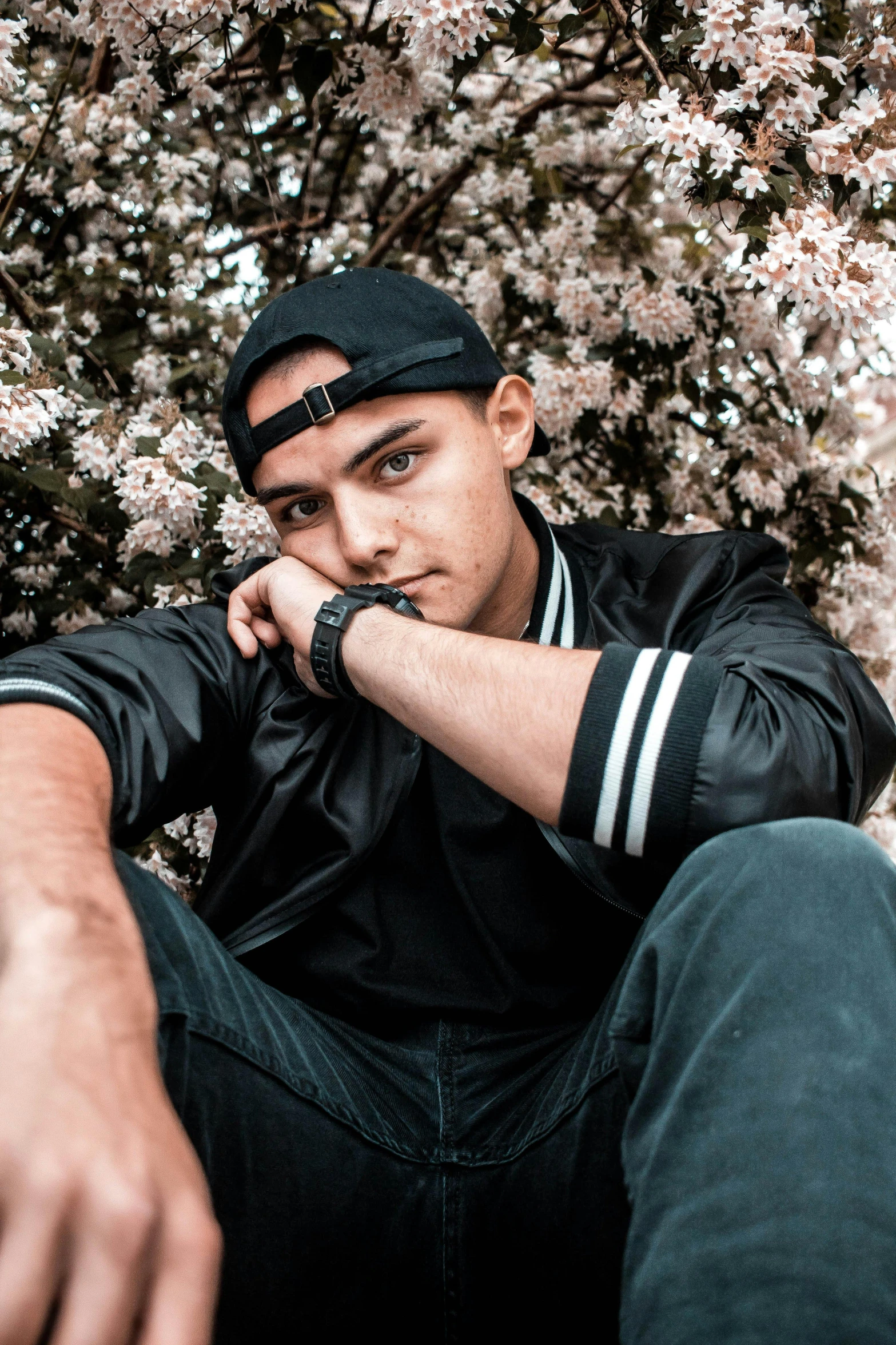 a man sitting in front of a bush of flowers, by Niko Henrichon, pexels contest winner, casual black clothing, male teenager, slightly tanned, charts