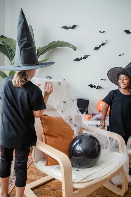 a couple of kids that are standing in a room, black witch hat, artificial spider web, kids playing, feature