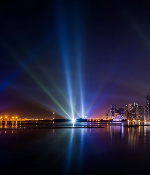 a large body of water with a city in the background, a hologram, by Ibrahim Kodra, pexels contest winner, moving heads light beams, today\'s featured photograph 4k, searchlight, subtle multicolored light