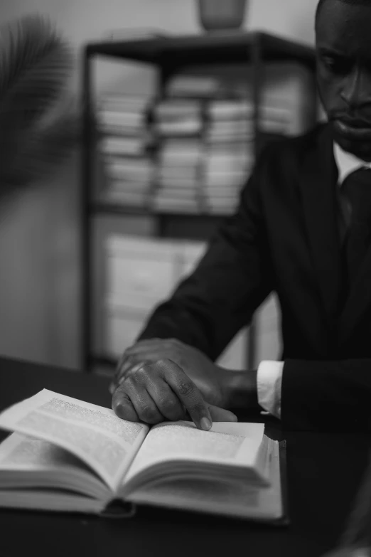 a man in a suit sitting at a desk with an open book, a black and white photo, unsplash, ((sharp focus)), black man, holding court, holding books