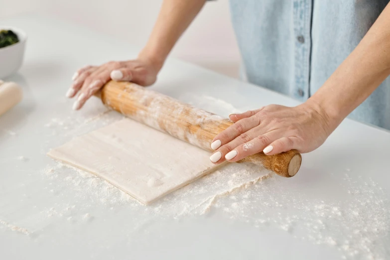 a person rolling out dough on a table, inspired by Sarah Lucas, trending on pexels, cream white background, holding a staff, gloss finish, wavy