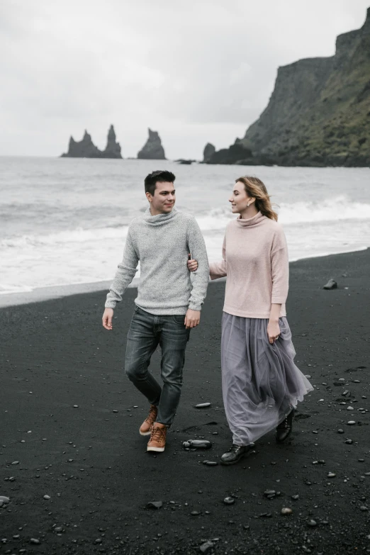 a man and woman walking on a black sand beach, by Hallsteinn Sigurðsson, pexels contest winner, renaissance, grey sweater, wearing a long flowy fabric, pastel hues, promotional image