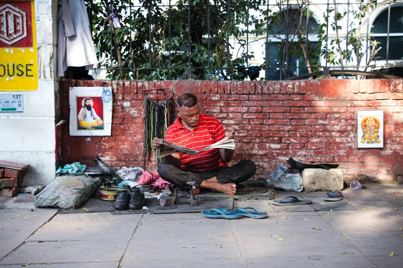 a man sitting on the sidewalk reading a book, by Ingrida Kadaka, pexels contest winner, bengal school of art, crafts and souvenirs, family photo, as well as the handyboy, a messy