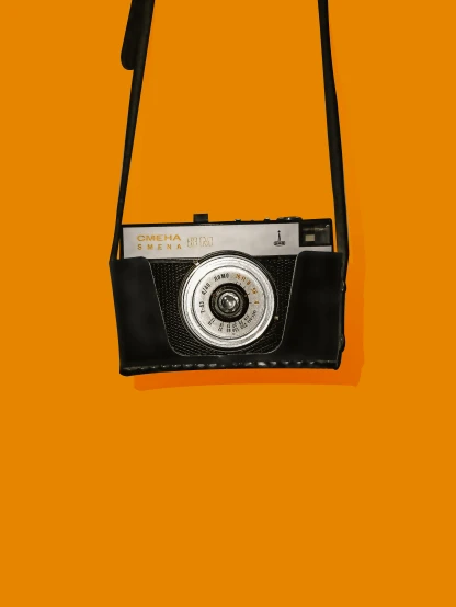a black camera sitting on top of an orange background, an album cover, inspired by Diane Arbus, bag, ((sharp focus)), society 6, may)