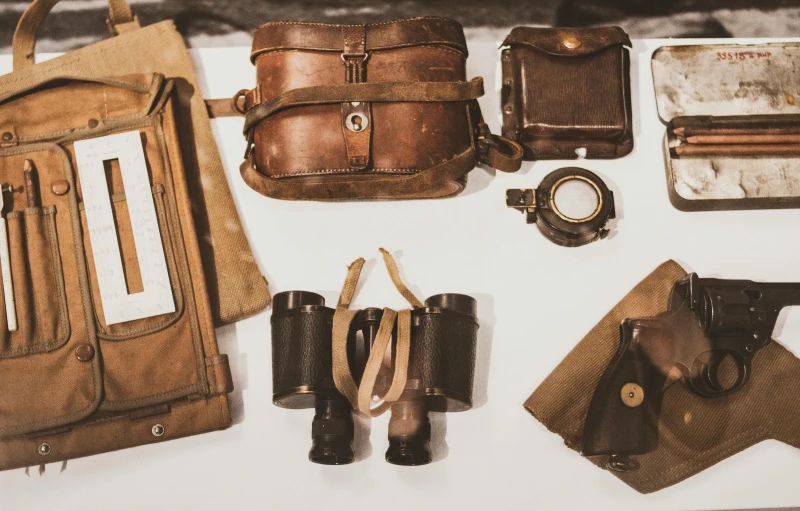 a bunch of items that are sitting on a table, binoculars, brown clothes, vintage - w 1 0 2 4, bags