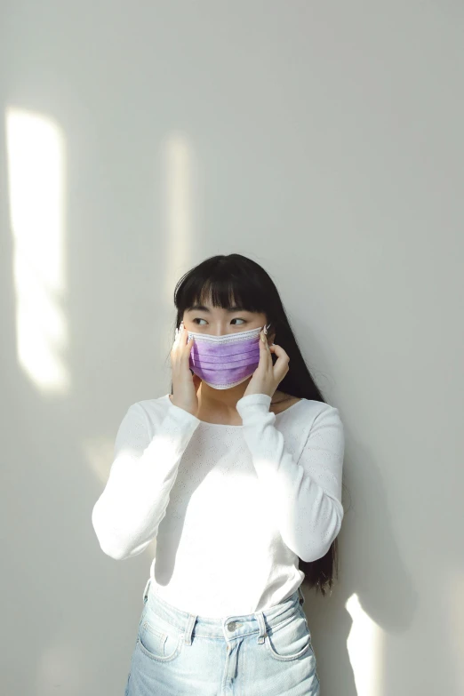 a woman in a white shirt and jeans talking on a cell phone, a picture, inspired by Yu Zhiding, trending on pexels, surgical mask covering mouth, wearing purple undershirt, in front of white back drop, asian human