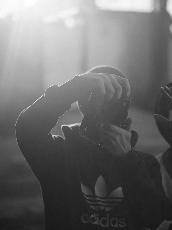 a black and white photo of a person wearing a hoodie, by Adam Marczyński, unsplash, behind the scenes, anamorphic lens flare, man in adidas tracksuit, hands shielding face