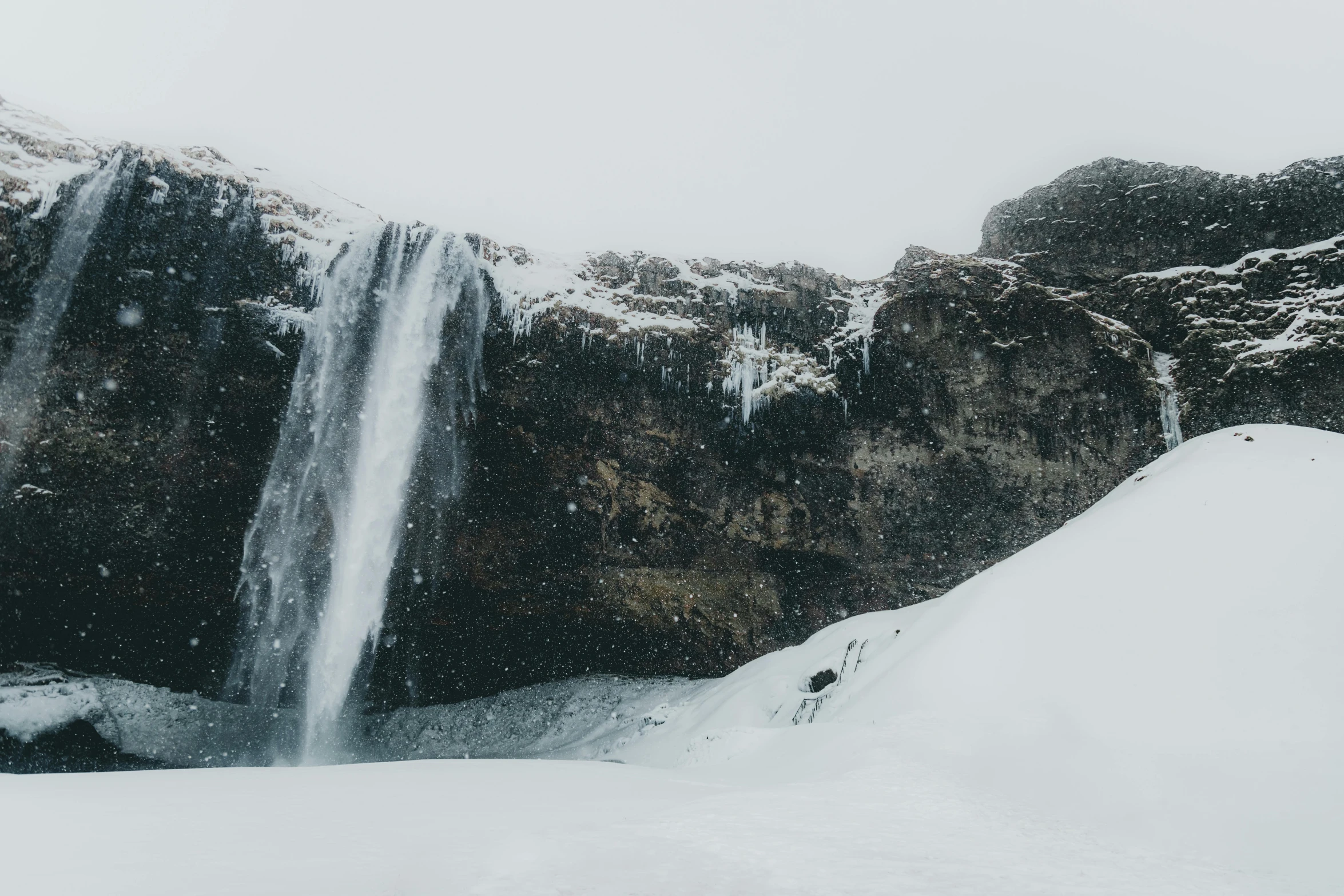 a man standing in front of a waterfall in the snow, pexels contest winner, hurufiyya, cut into the side of a mountain, 4 k hd wallpapear, distant photo, small waterfall