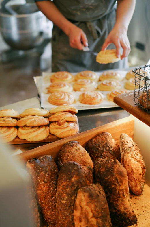 a person standing in front of a counter filled with pastries, by Elizabeth Durack, pexels, process art, warm light, bread, new zealand, crispy buns