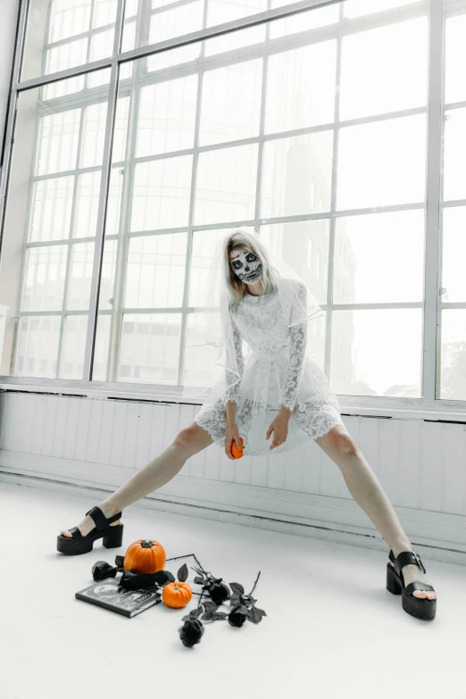 a woman in a white dress standing in front of a window, an album cover, inspired by Elsa Bleda, pexels contest winner, conceptual art, skulls at her hips, full body robot with human mask, sitting on the floor, trick or treat