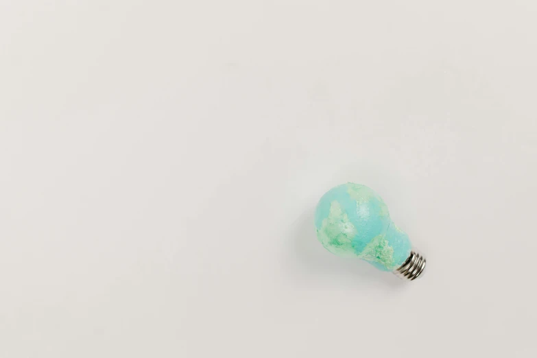 a light bulb sitting on top of a white surface, by Ryan Pancoast, unsplash, conceptual art, with celadon glaze, tie-dye, resin and clay art, high - angle view