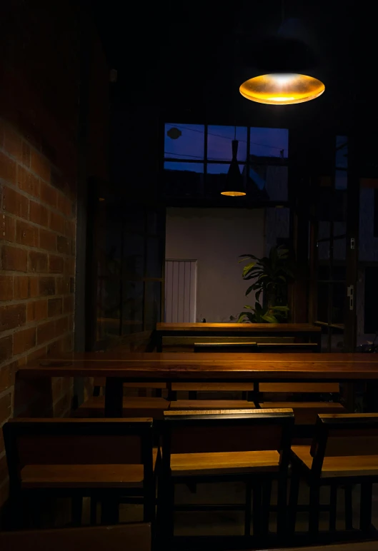 a row of wooden benches sitting next to a brick wall, light and space, cafe lighting, dark hazy room, distant photo, atmospheric lighting - n 9