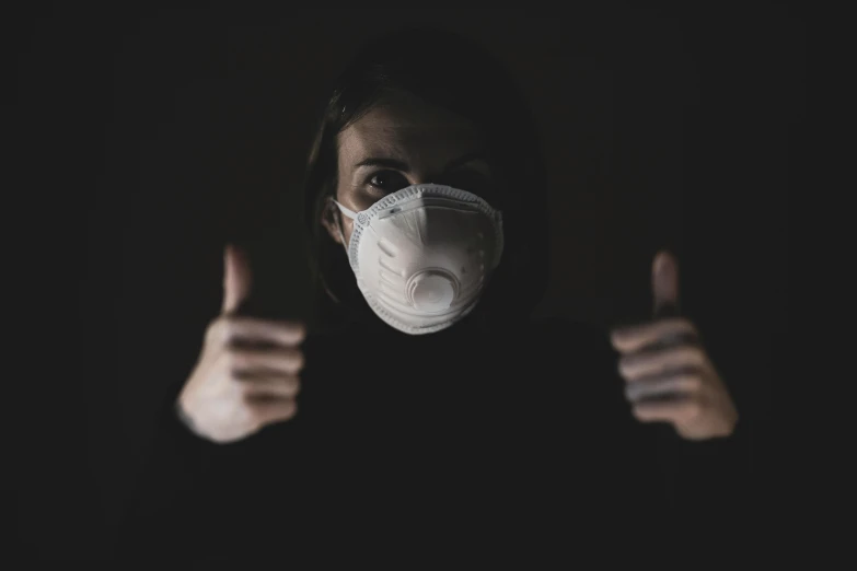 a woman wearing a face mask and thumbs up, by Adam Marczyński, pexels contest winner, dark and dusty, background image, virus, dark and white