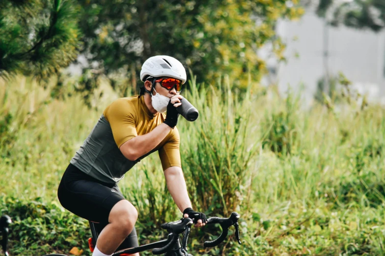 a man riding a bike while talking on a cell phone, hydration, visor over face, gold, 1/2 pro mist filter