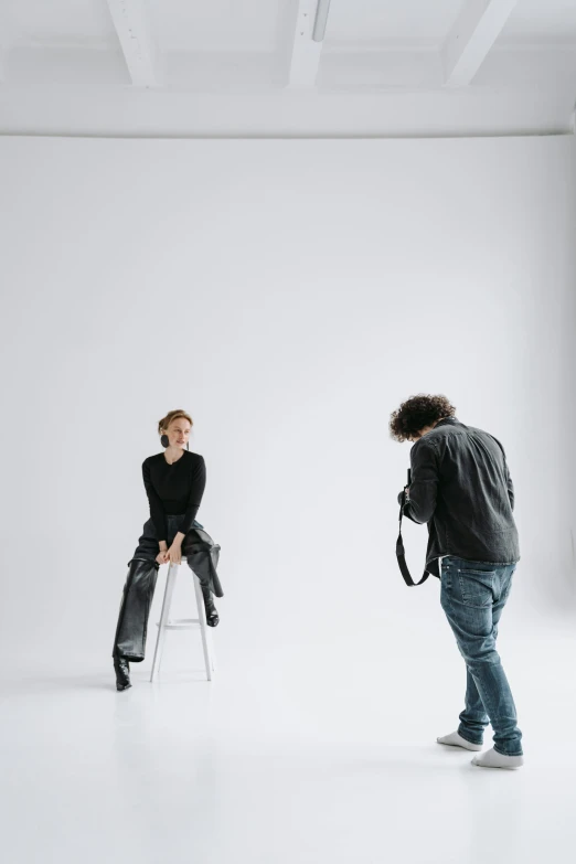 a man taking a picture of a woman in a white room, by Tom Bonson, trending on unsplash, sitting on a stool, dark grey backdrop studio, full body shoot, high detailed photography cape