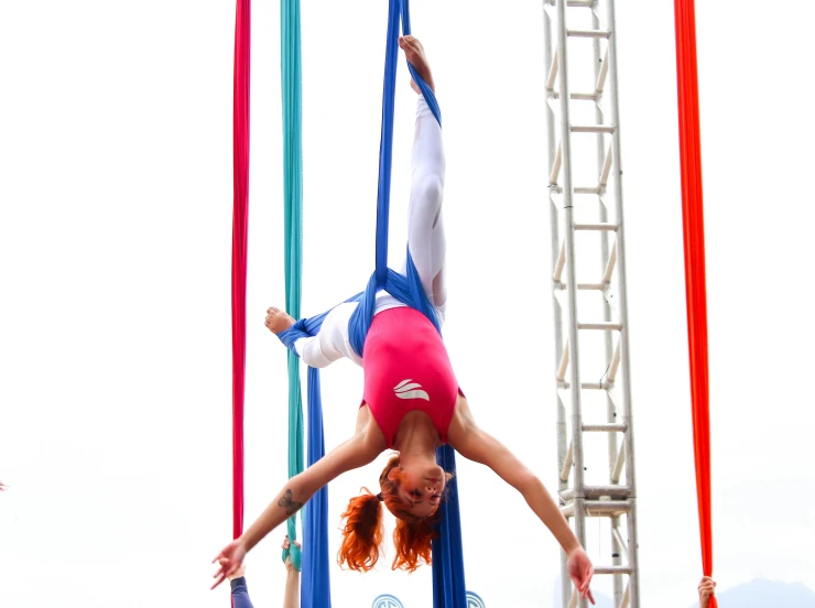 a woman flying through the air on top of a pole, inspired by The Family Circus, pexels contest winner, arabesque, ribbons, in a colorful tent, harnesses, square