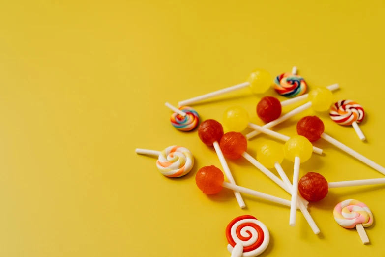 a pile of lollipops sitting on top of a yellow surface, trending on pexels, background image, “berries, swirly tubes, miniatures