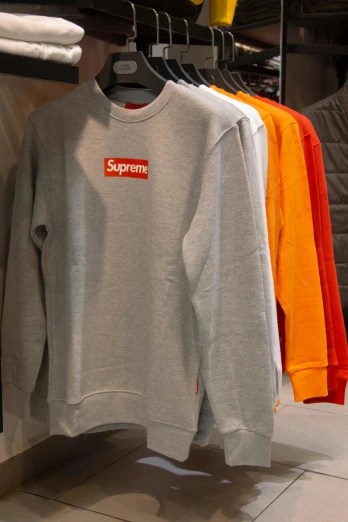 a supreme sweatshirt hanging on a rack in a store, happening, gray and orange colours, thumbnail