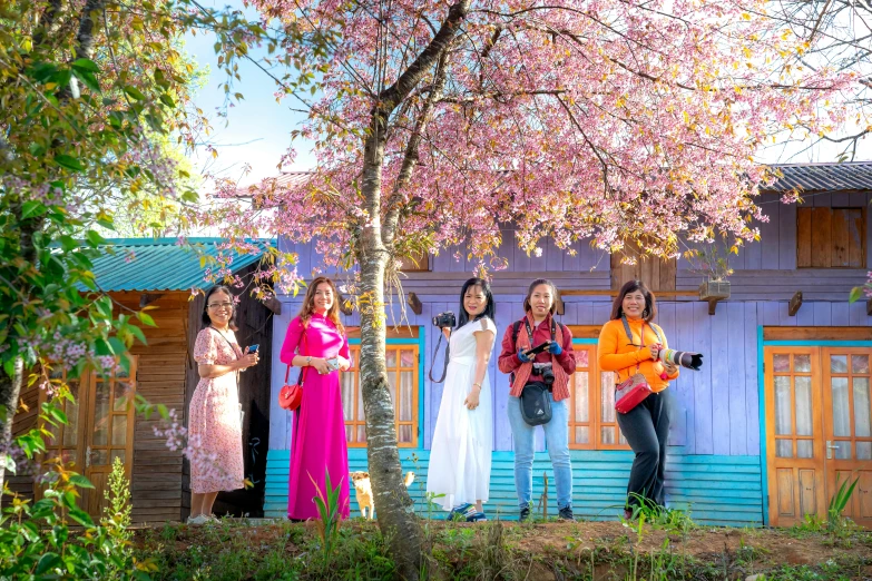 a group of people standing in front of a building, by Aya Goda, pexels contest winner, cherry blossom forest, cottagecore hippie, brightly coloured, in style of lam manh